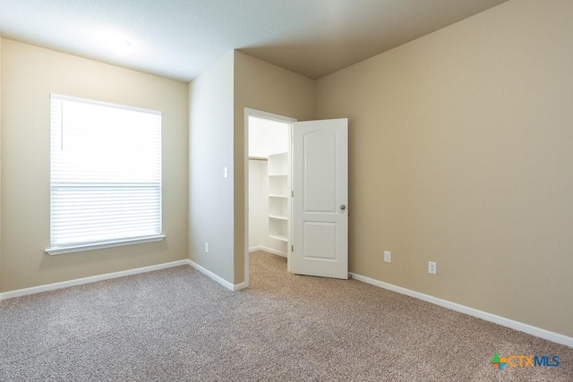 unfurnished bedroom featuring a walk in closet and light colored carpet