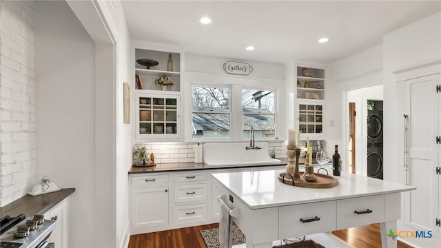 kitchen with a kitchen bar, sink, white cabinetry, stacked washer and clothes dryer, and dark hardwood / wood-style flooring