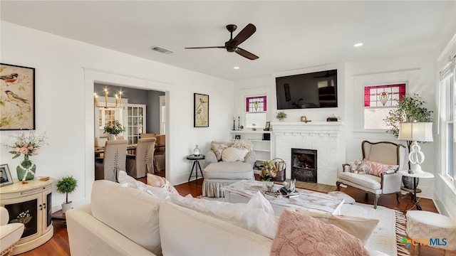 living room with ceiling fan with notable chandelier, hardwood / wood-style floors, and a fireplace