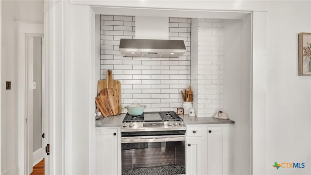 kitchen featuring ventilation hood, gas stove, white cabinets, and backsplash