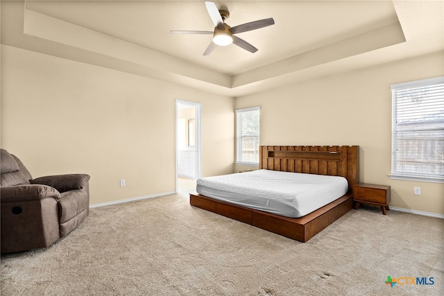 bedroom featuring light colored carpet, ceiling fan, a tray ceiling, and connected bathroom