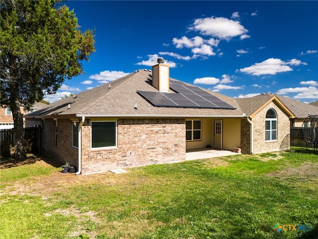 rear view of house with solar panels, a lawn, and a patio area