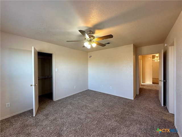 unfurnished bedroom featuring dark colored carpet, ceiling fan, a walk in closet, and a textured ceiling