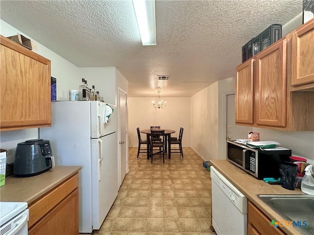 kitchen featuring a textured ceiling, white appliances, sink, decorative light fixtures, and a chandelier