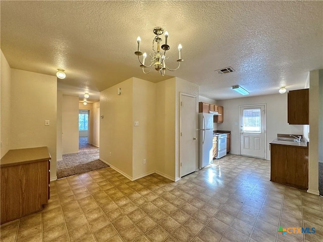 kitchen featuring white appliances, a textured ceiling, a notable chandelier, and sink