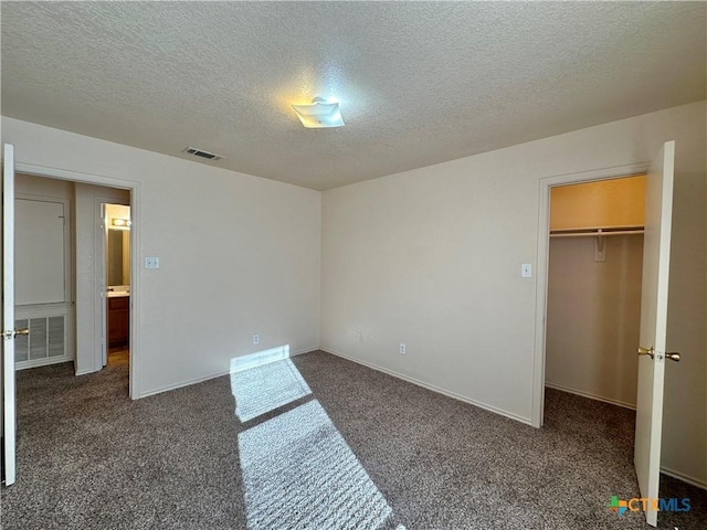 unfurnished bedroom with a walk in closet, a closet, a textured ceiling, and dark colored carpet