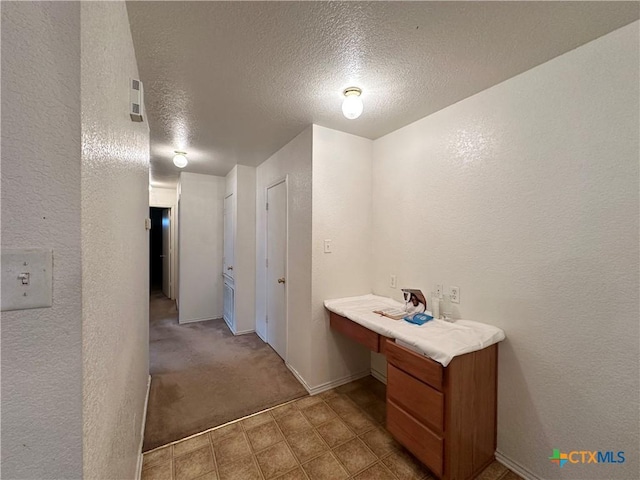 hallway with a textured ceiling and light carpet