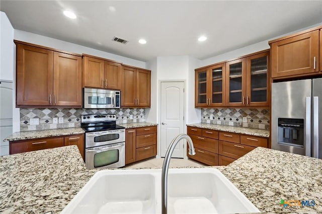 14424 Tuscola Cir, Austin, TX 78734 - kitchen with stainless steel appliances, backsplash, glass insert cabinets, brown cabinetry, and recessed lighting