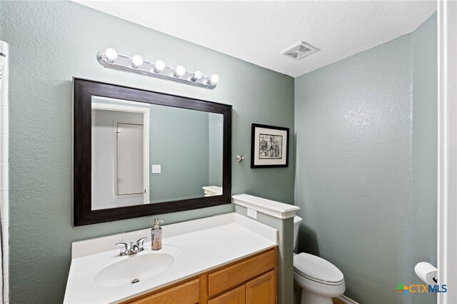 bathroom with a textured ceiling, vanity, and toilet