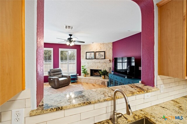 living room featuring a stone fireplace, ceiling fan, and hardwood / wood-style flooring