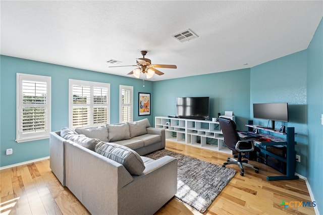 living room featuring ceiling fan, light hardwood / wood-style floors, and a textured ceiling