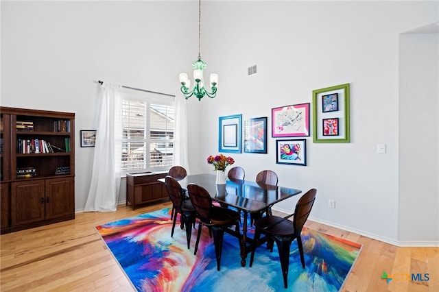 dining space featuring a towering ceiling, light hardwood / wood-style floors, and a notable chandelier