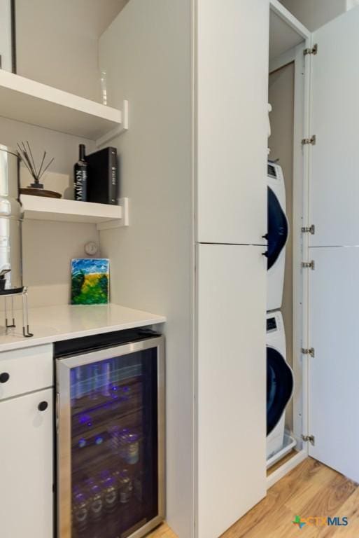 bar with white cabinetry, stacked washing maching and dryer, wine cooler, and light hardwood / wood-style floors