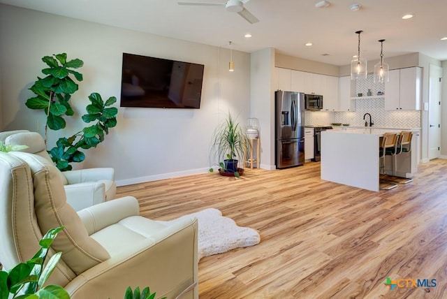 living room with sink, light hardwood / wood-style floors, and ceiling fan