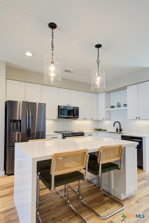 kitchen featuring appliances with stainless steel finishes, hanging light fixtures, a kitchen island, and white cabinets