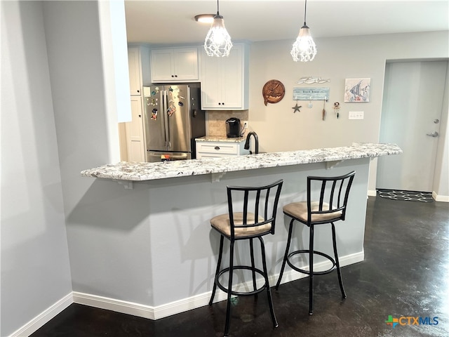 kitchen featuring pendant lighting, stainless steel refrigerator, a breakfast bar, and white cabinets