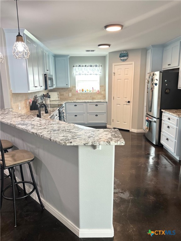 kitchen with stainless steel appliances, decorative light fixtures, a kitchen bar, decorative backsplash, and kitchen peninsula