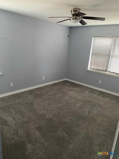 empty room with dark carpet, a ceiling fan, and baseboards