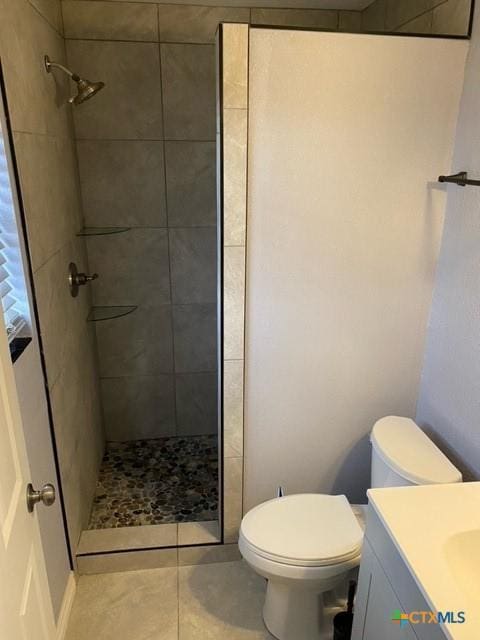 full bathroom featuring tile patterned flooring, toilet, vanity, and a tile shower