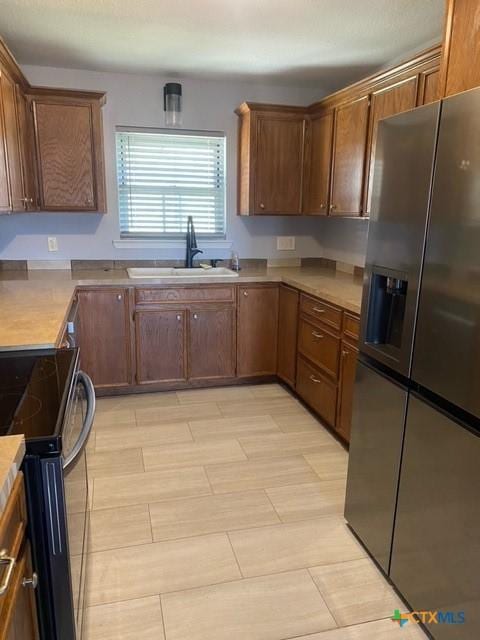 kitchen with light countertops, stainless steel fridge with ice dispenser, range with electric stovetop, and a sink