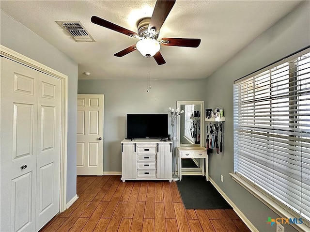 interior space featuring baseboards, visible vents, ceiling fan, and wood finished floors