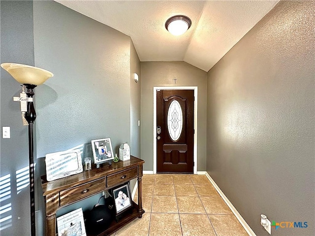 entrance foyer featuring a textured wall, light tile patterned flooring, vaulted ceiling, a textured ceiling, and baseboards