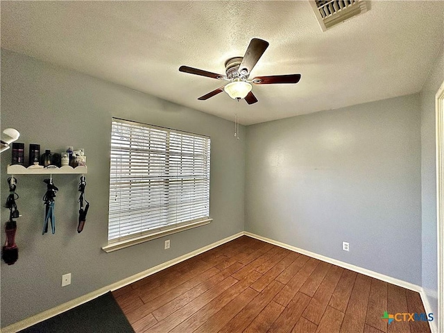 empty room with a textured ceiling, a ceiling fan, visible vents, baseboards, and dark wood finished floors