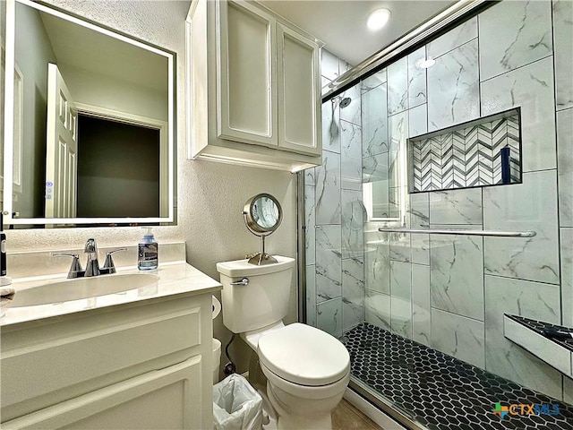 bathroom with a stall shower, a textured wall, vanity, and toilet