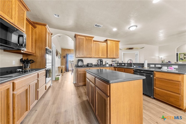 kitchen with sink, black appliances, kitchen peninsula, light hardwood / wood-style flooring, and a center island