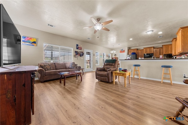 living room with light hardwood / wood-style floors, ceiling fan, and a textured ceiling