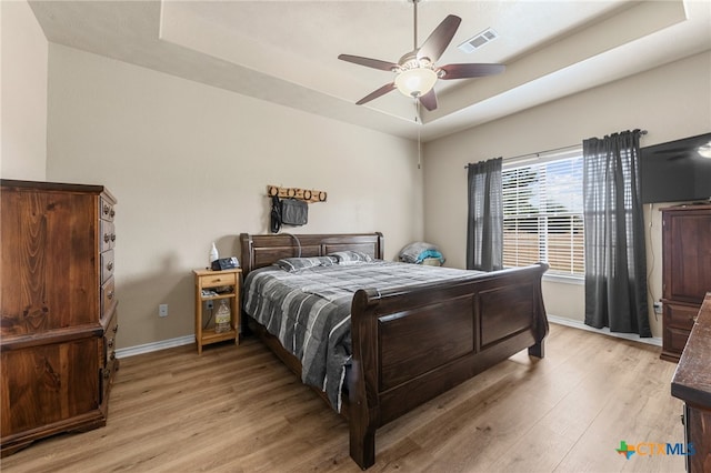 bedroom featuring a raised ceiling, ceiling fan, and light hardwood / wood-style flooring