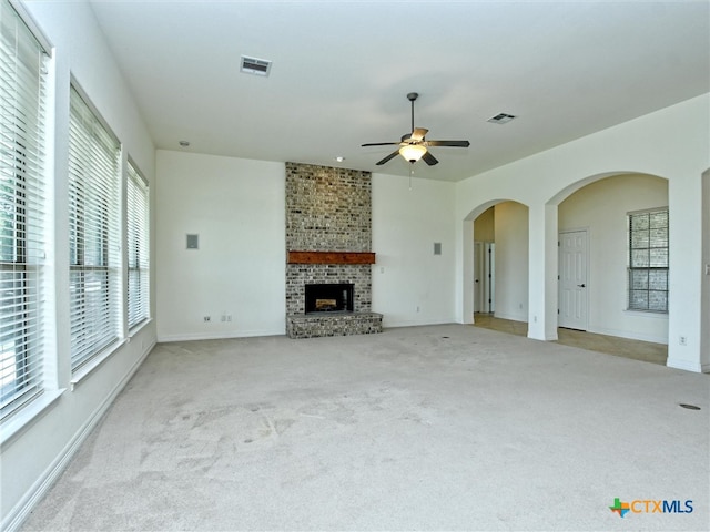 unfurnished living room with a brick fireplace, light colored carpet, a healthy amount of sunlight, and ceiling fan