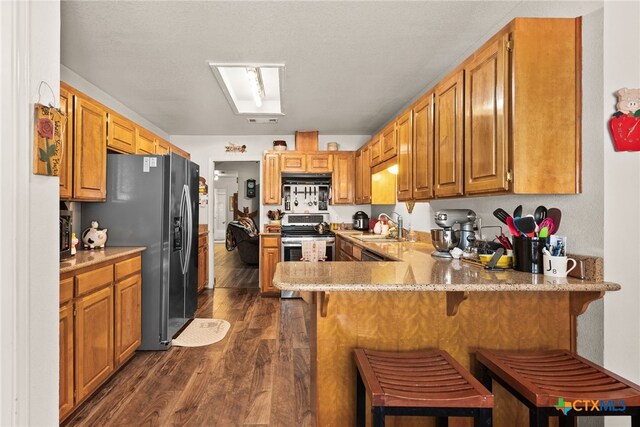 kitchen with a breakfast bar, sink, appliances with stainless steel finishes, dark hardwood / wood-style floors, and kitchen peninsula