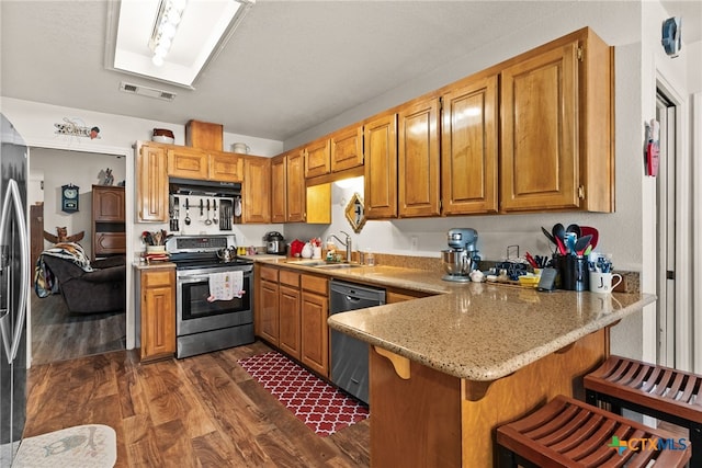 kitchen featuring dark wood-type flooring, a kitchen bar, sink, kitchen peninsula, and stainless steel appliances