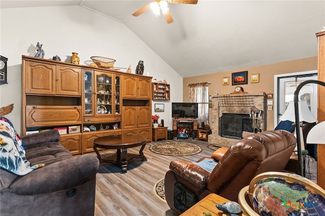 living room featuring a brick fireplace, vaulted ceiling, ceiling fan, and light wood-type flooring