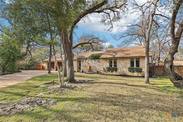 single story home featuring stone siding, concrete driveway, a front yard, and fence