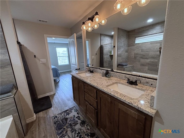 bathroom featuring visible vents, wood finished floors, baseboards, a sink, and a tile shower