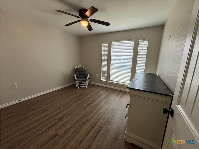 unfurnished office with dark wood-type flooring, a ceiling fan, and baseboards