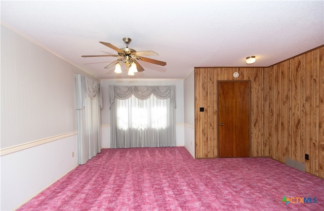 empty room featuring carpet flooring, ornamental molding, a textured ceiling, ceiling fan, and wooden walls