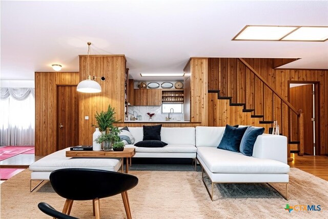 living room featuring sink, light wood-type flooring, and wood walls