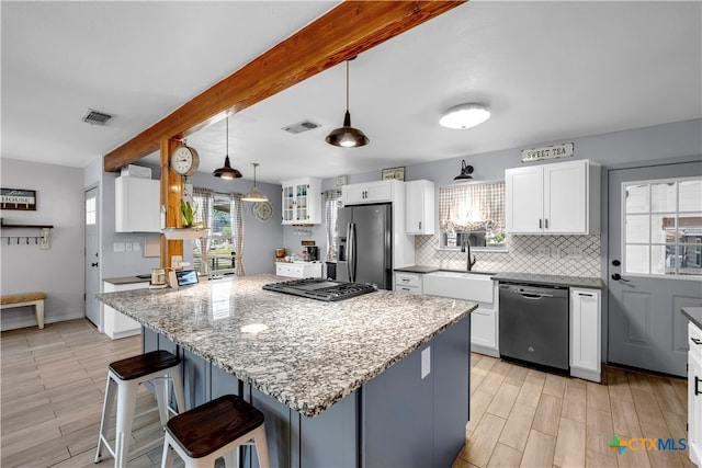 kitchen with stainless steel appliances, a wealth of natural light, white cabinetry, and a center island