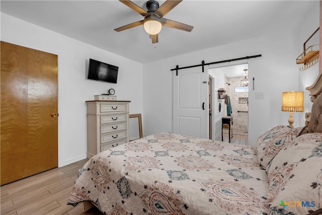 bedroom with ensuite bathroom, a barn door, ceiling fan, and light hardwood / wood-style flooring