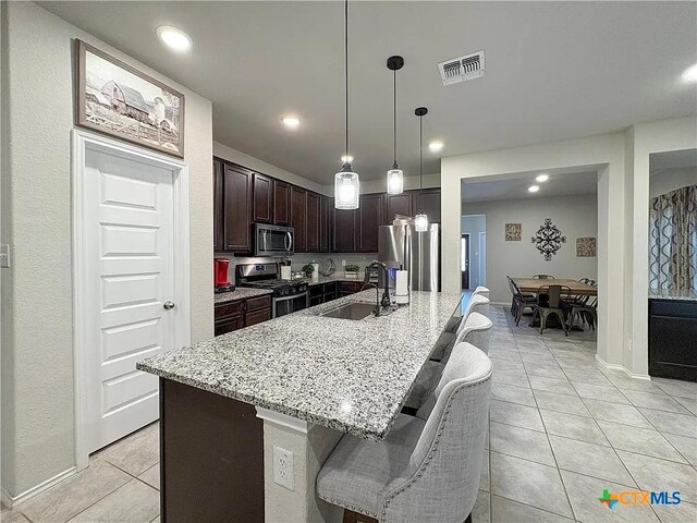 kitchen with dark brown cabinets, stainless steel appliances, an island with sink, sink, and a kitchen bar