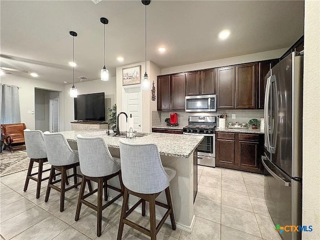 kitchen with a kitchen island with sink, stainless steel appliances, sink, a kitchen bar, and pendant lighting