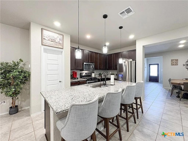 kitchen featuring hanging light fixtures, stainless steel appliances, sink, dark brown cabinets, and a kitchen breakfast bar