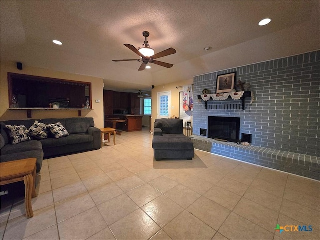 living area with light tile patterned flooring, a brick fireplace, a textured ceiling, a ceiling fan, and recessed lighting