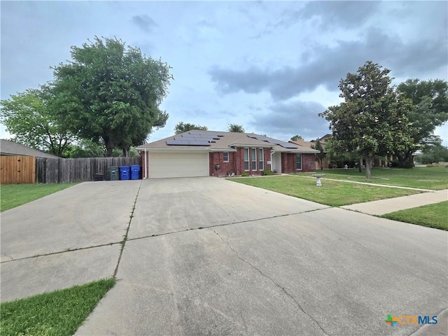 ranch-style home featuring driveway, solar panels, a front yard, a garage, and brick siding
