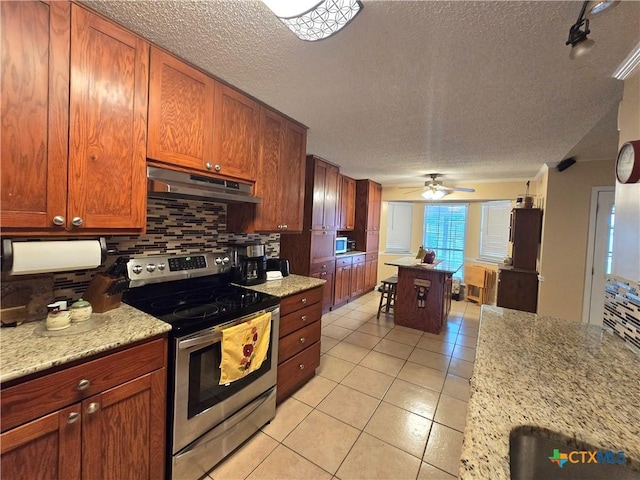 kitchen with appliances with stainless steel finishes, a textured ceiling, backsplash, light tile patterned floors, and under cabinet range hood