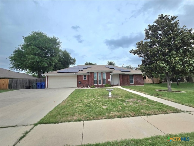 single story home featuring brick siding, roof mounted solar panels, a front lawn, concrete driveway, and an attached garage