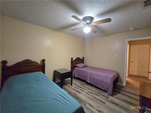 bedroom with a textured ceiling, a ceiling fan, baseboards, wood finished floors, and visible vents